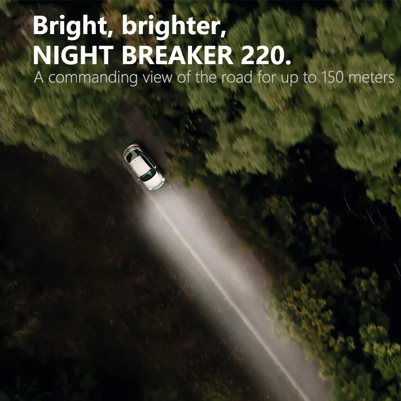 Car driving on a road with headlights illuminating the path through a forest, featuring text about the 'NIGHT BREAKER 220'.